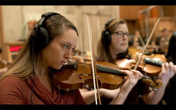 Aiva gallery image showing musicians playing violins in a recording studio, highlighting human performance of AI-composed music.