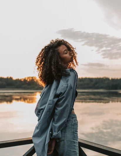 Clipdrop photo enhancement example showing a woman with curly hair silhouetted by golden hour light over a lake.