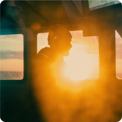 Cohere brand image showing a person in silhouette wearing headphones, looking out at a golden sunset from inside a boat cabin, conveying exploration.