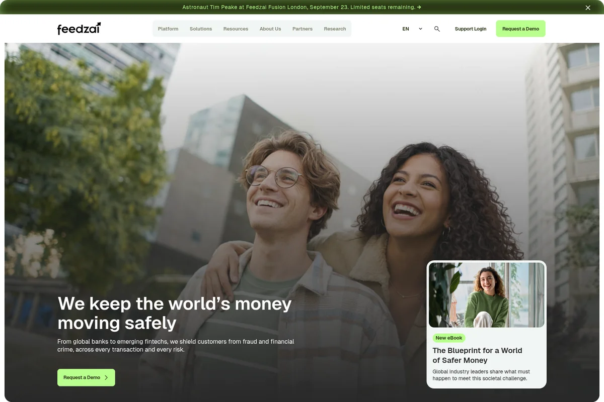 Feedzai homepage hero section showing two smiling people and a headline about keeping money safe, within a modern web interface.