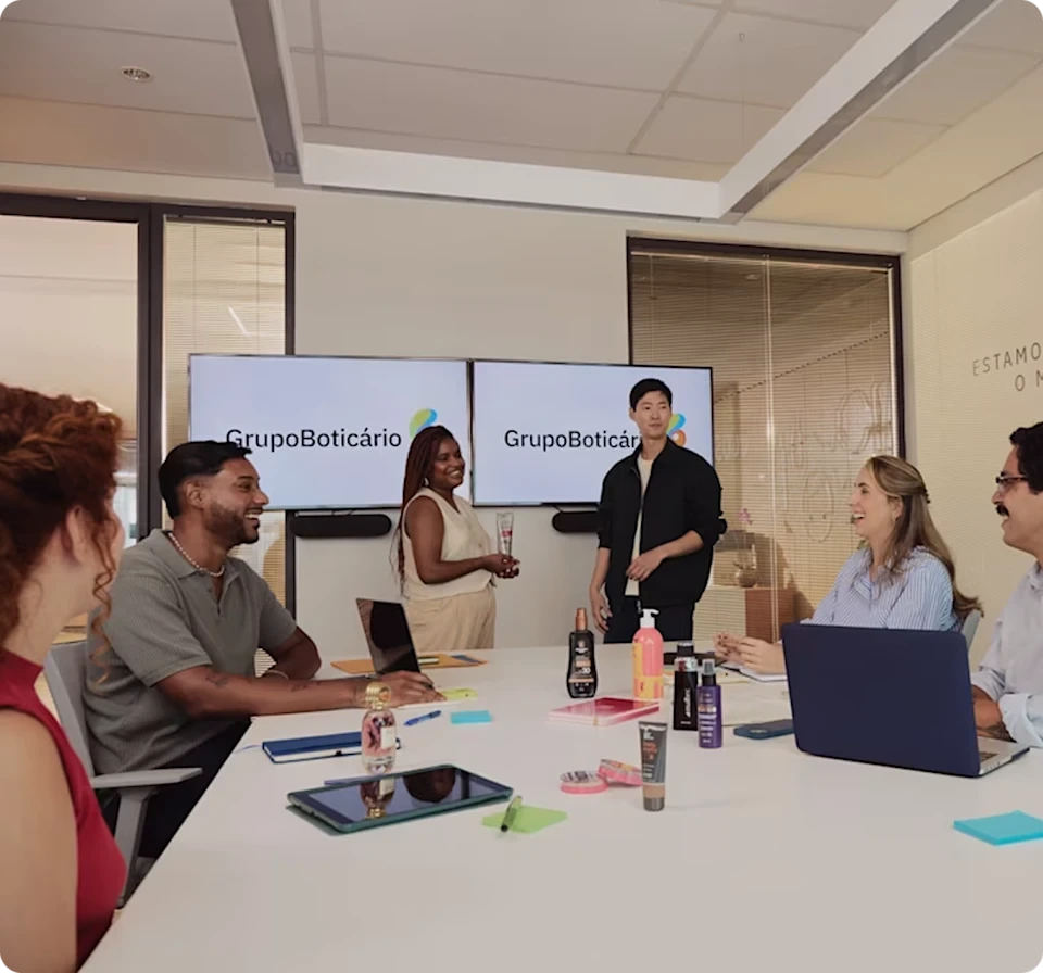 Grupo Boticário marketing meeting showing team members discussing beauty products with brand logos on screens
