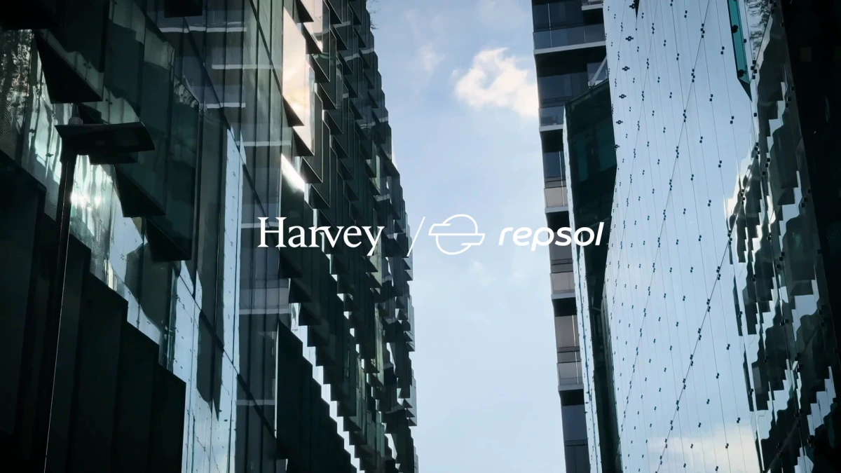 Harvey and Repsol partnership branding against modern glass skyscrapers and a blue sky.