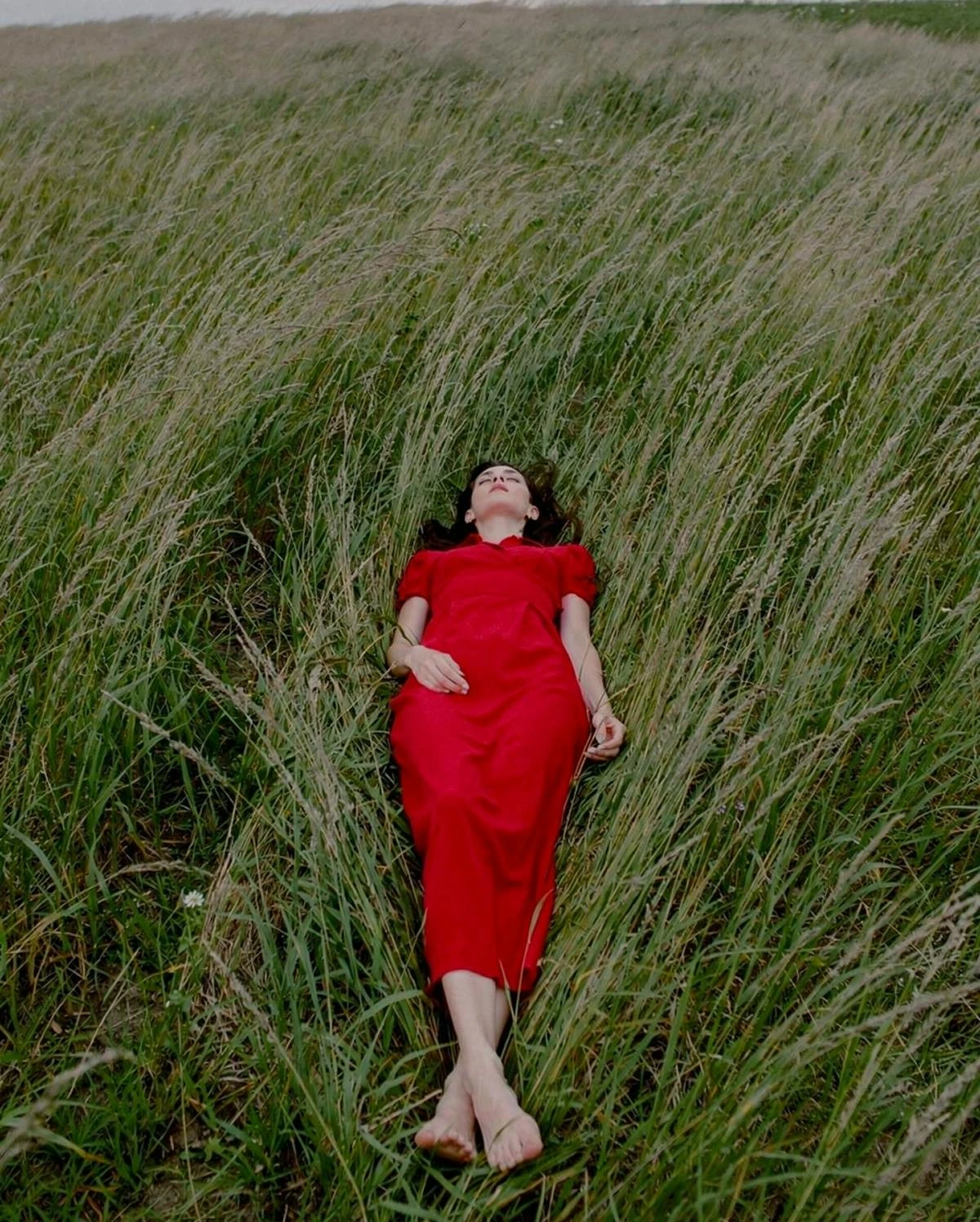 Leonardo AI generated image showing a person in a red dress lying in a field of tall green grass, demonstrating photorealistic capabilities.