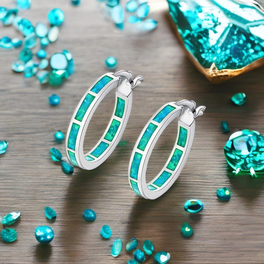 Pebblely output sample showing two hoop earrings with blue-green opal inlay and scattered gemstones on a wooden surface.