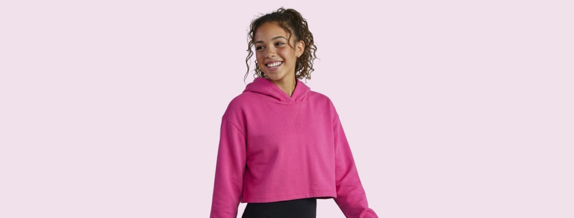 Photoroom output sample showing a smiling person wearing a bright pink cropped hoodie on a clean light pink background.