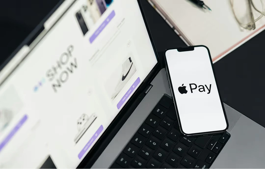 A laptop displaying an e-commerce website with product listings and 'Add to Cart' buttons, next to a smartphone showing the Apple Pay logo for convenient mobile payment.