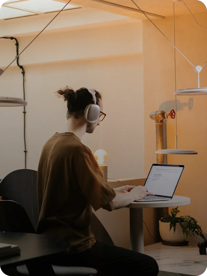 Wellsaid Labs user wearing headphones, typing on a laptop, demonstrating focused content creation in a modern office.